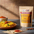 Biryani Masala spice blend pouch beside a bowl of biryani rice, with scattered whole spices on a cloth.