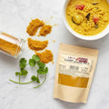 Curry Powder Mild pouch on a marble surface with spilled curry powder, coriander sprigs, and a bowl of curry.
