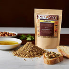 Dukkah spice blend pouch behind a pile of dukkah, with olive oil dip and toasted bread slices