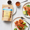 Fish Masala pouch with plated salmon and prawns, lime wedges, and small bowls of sauce and spice.