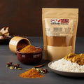 Garam masala pouch beside a bowl and pile of ground spice, whole spices, rice, and curry on a dark surface.