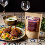 Ras el Hanout pouch beside a plate of lamb chops with citrus salad, with a bowl of yogurt on a patterned table.