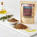 Za’atar pouch beside a bowl and pile of za’atar on a white board, with olive oil and herb sprigs in the background.