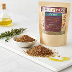 Za’atar pouch beside a bowl and pile of za’atar on a white board, with olive oil and herb sprigs in the background.